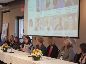 Panel of women at an event with projector screen in background