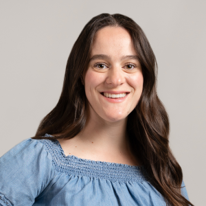 Christy smiling wearing a blue dress in front of a grey background