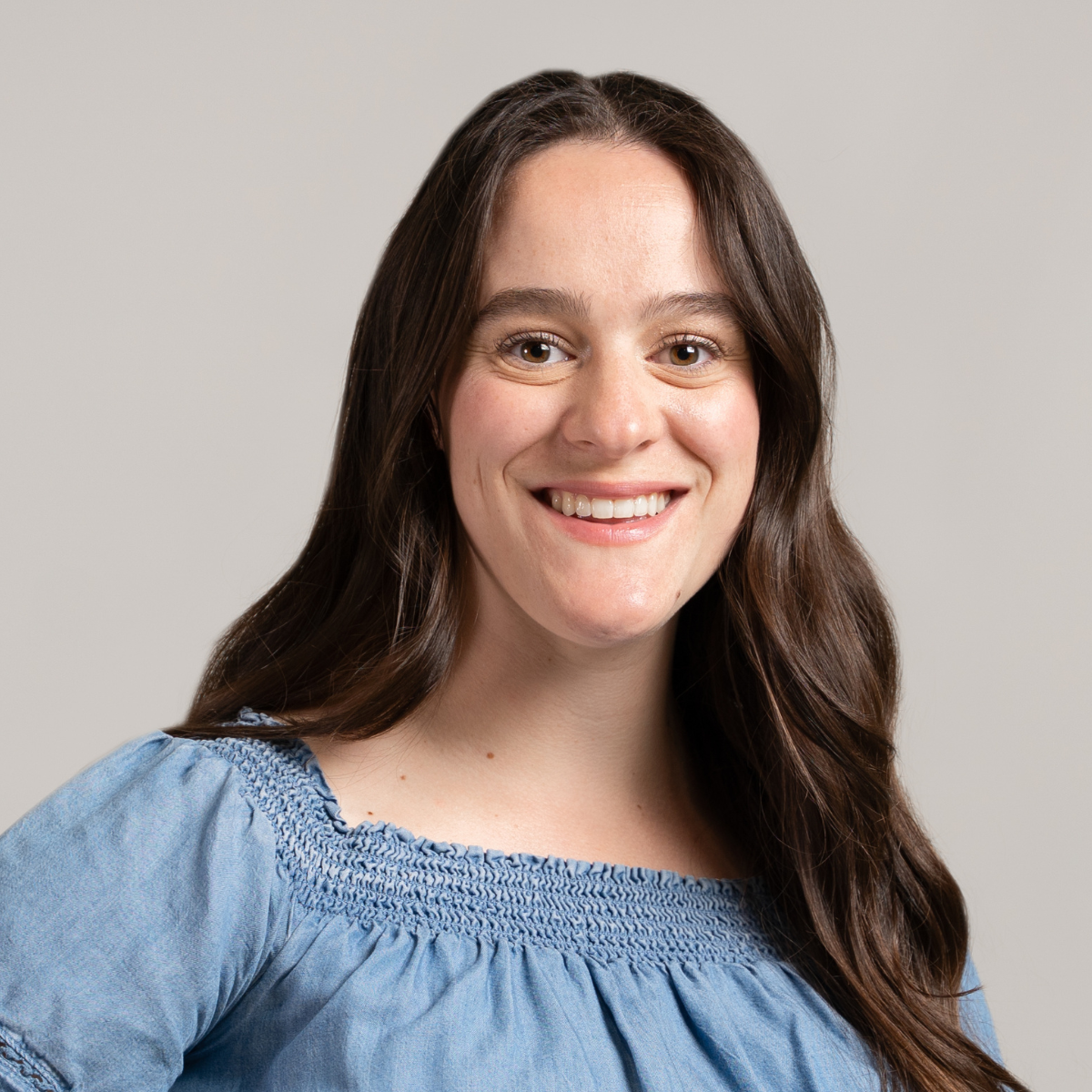 Christy smiling wearing a blue dress in front of a grey background