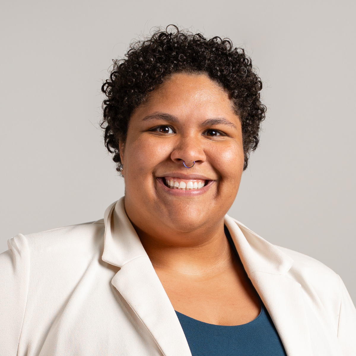 Endira smiling headshot wearing a white blazer and blue undershirt in front of a grey background