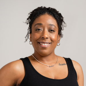 Jade smiling wearing a black tank top in front of a grey background