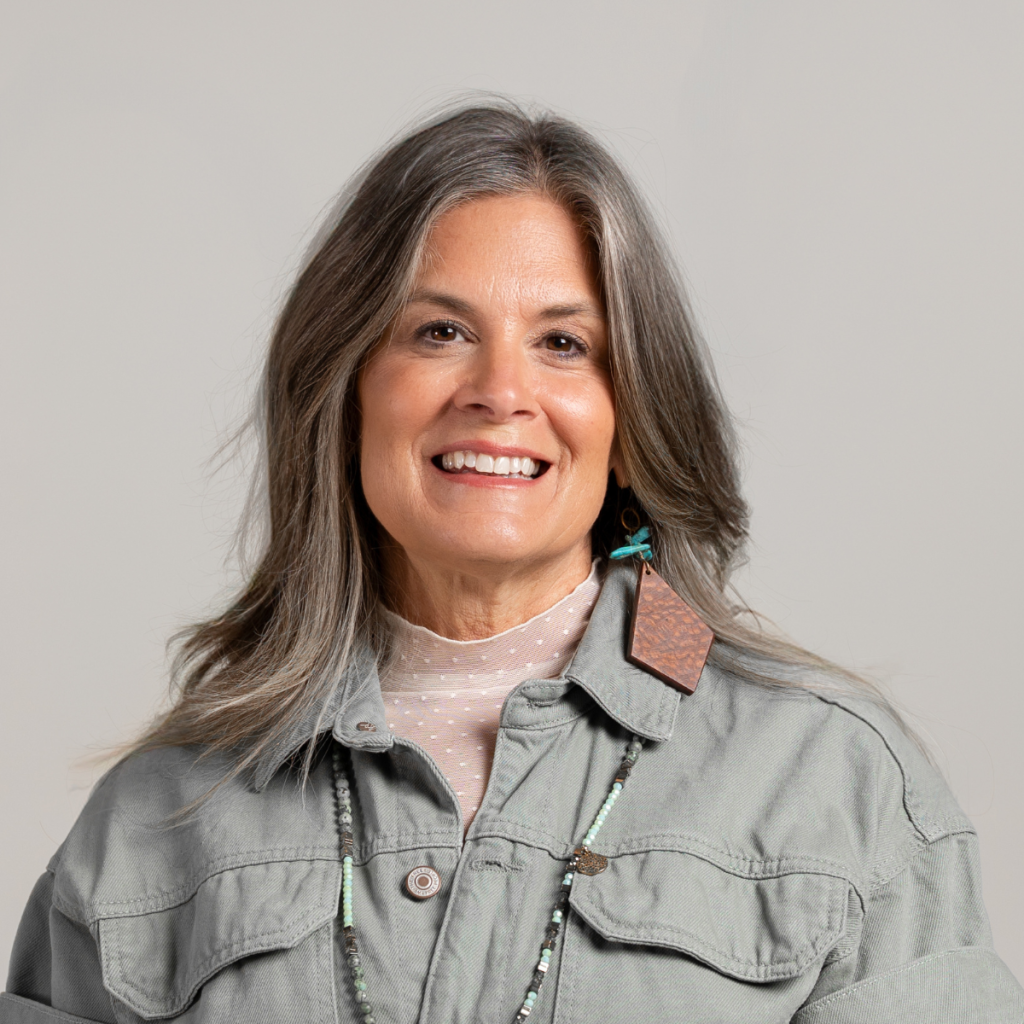 Krista Batdorff, Bed Rest & Postpartum Doulas, of Gold Coast Doulas poses against a grey backdrop wearing a grey denim jacket headshot