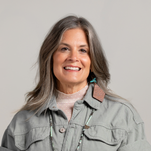 Krista Batdorff, Bed Rest & Postpartum Doulas, of Gold Coast Doulas poses against a grey backdrop wearing a grey denim jacket headshot