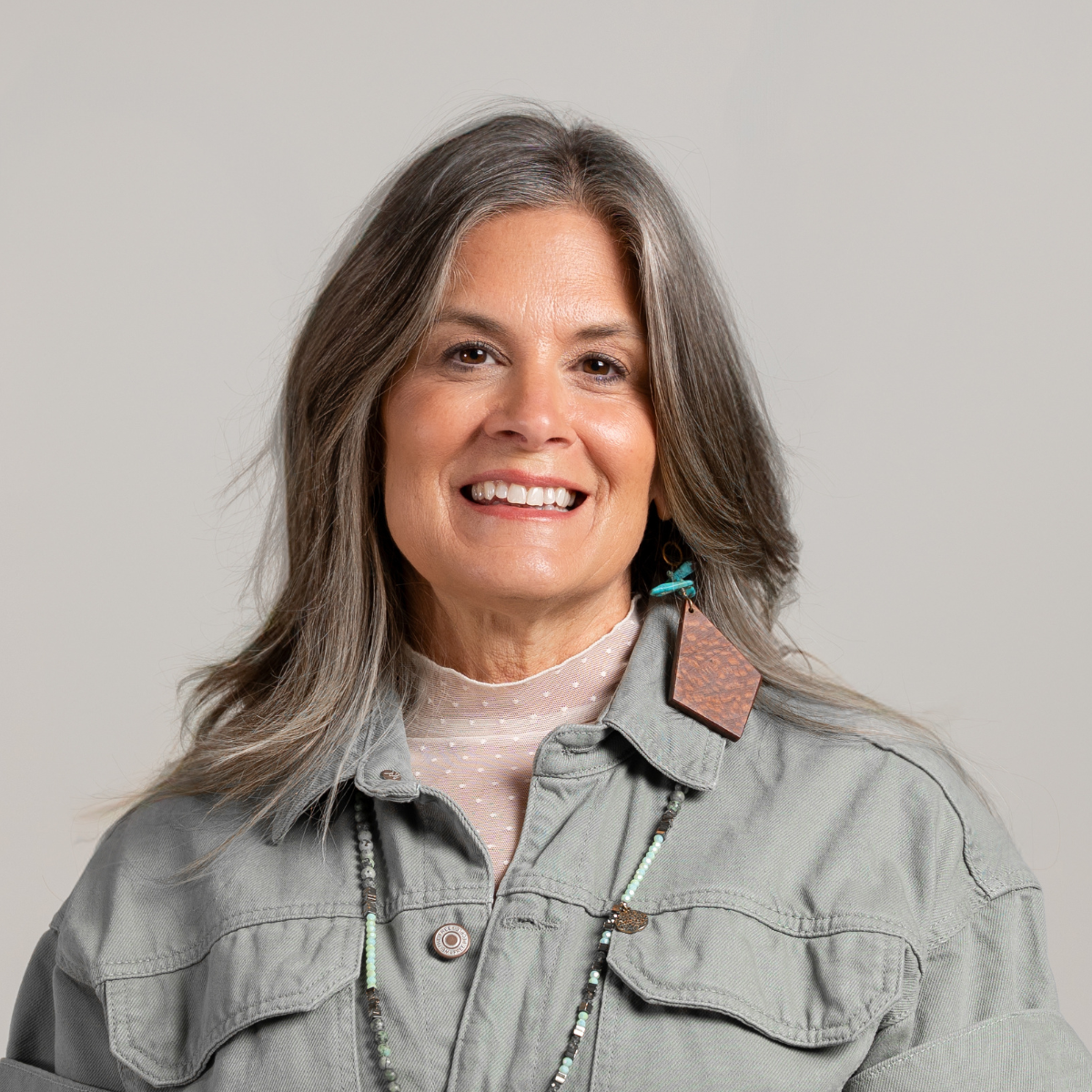 Krista Batdorff, Bed Rest & Postpartum Doulas, of Gold Coast Doulas poses against a grey backdrop wearing a grey denim jacket headshot