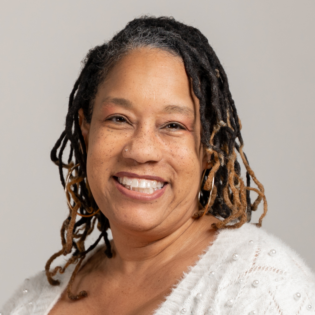 LaVita smiling wearing a white shirt in front of a grey background