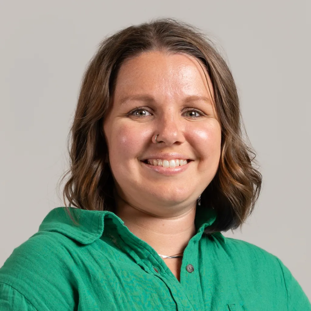 Sara smiling wearing a green shirt in front of a grey background