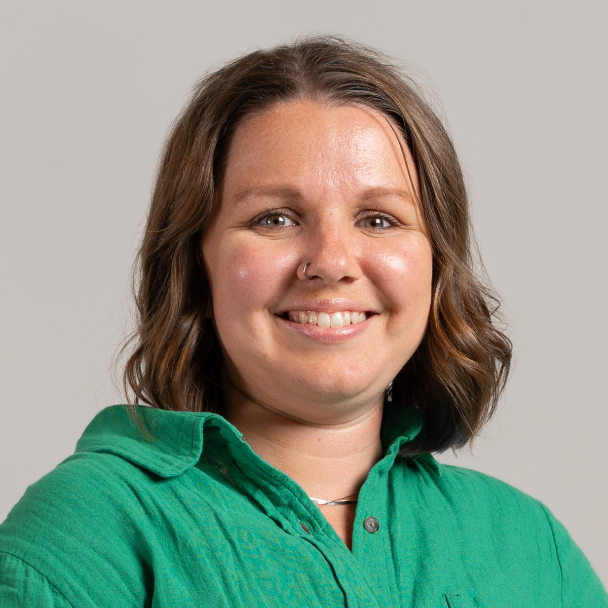 Sara smiling wearing a green shirt in front of a grey background