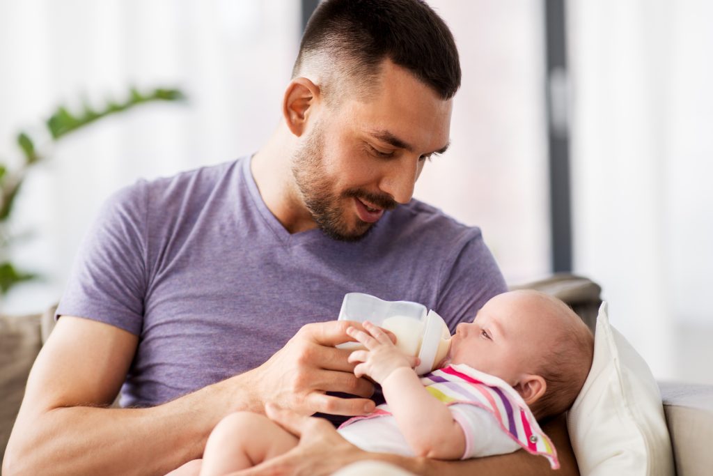 father feeding baby daughter from bottle at home