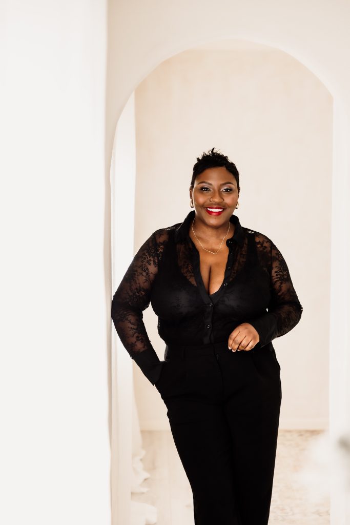 Smiling woman with short hair in a black lace blouse standing in a white doorway archway.